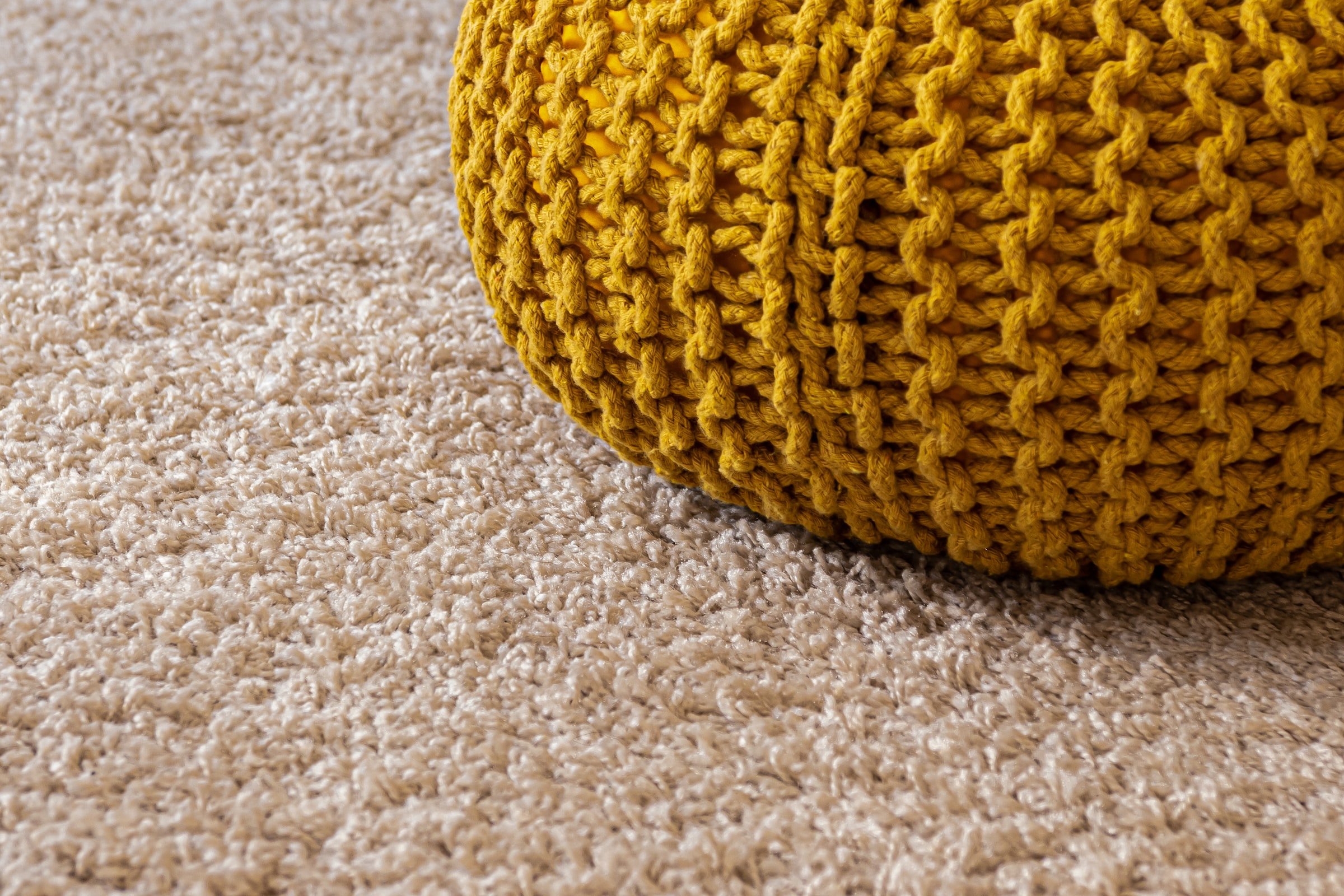 Beige carpet flooring under a yellow ottoman